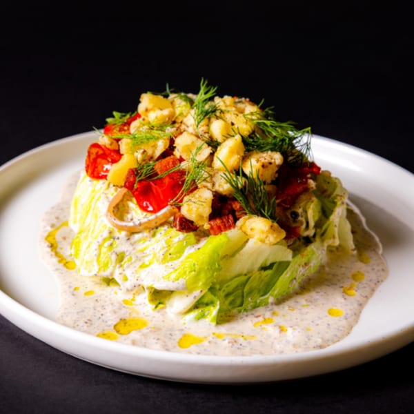 Wedge salad with creamy dressing, red tomatoes, croutons, and fresh dill on a white plate.