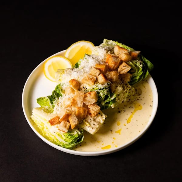 Caesar salad with romaine lettuce, croutons, parmesan cheese, dressing, and lemon wedges on a white plate.