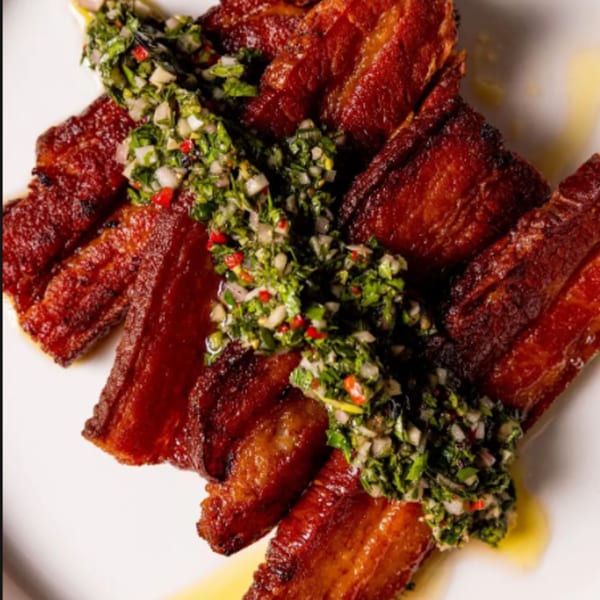 Crispy pork belly strips topped with vibrant green chimichurri sauce on a white plate.