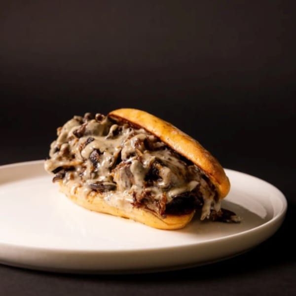 A mushroom and cheese sandwich on a white plate against a dark background.